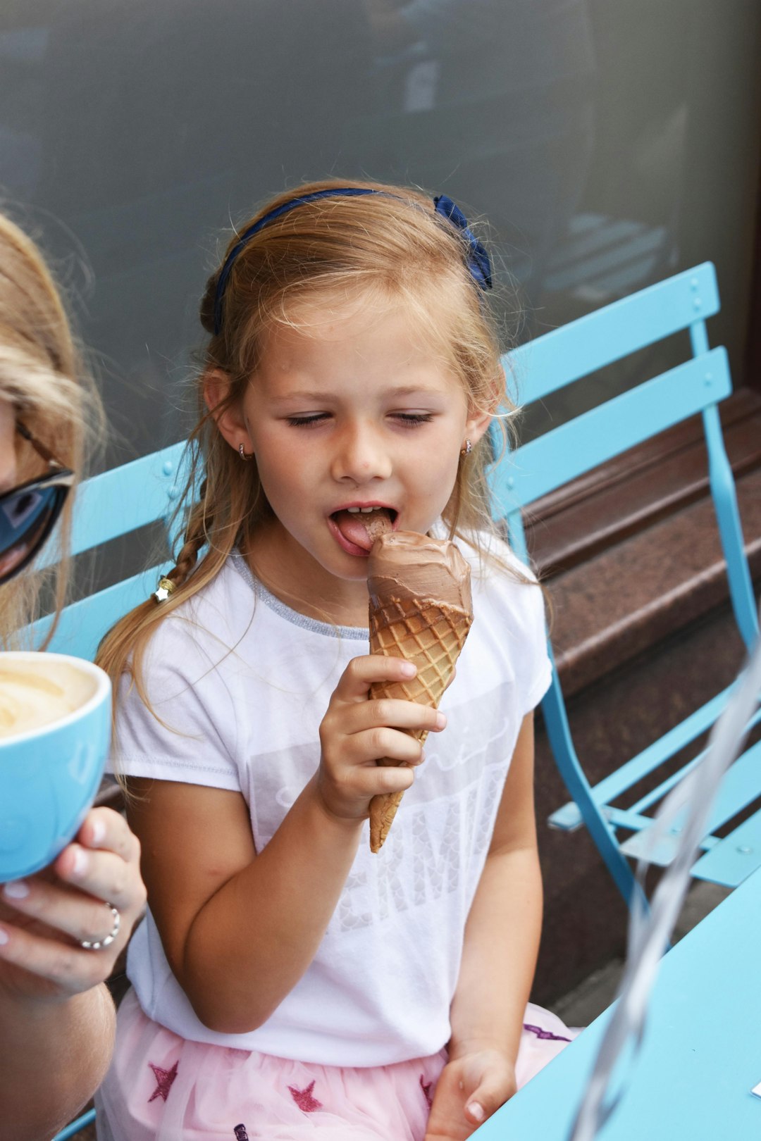 Small girl eating chocolate ice-cream in a cone outside a cafe.